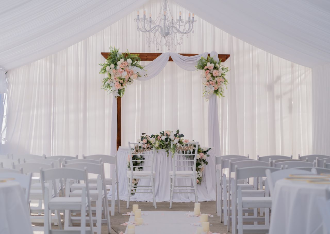 Beautiful wedding ceremony setup with white drapery, floral arrangements, and chandelier. Perfect for elegant nuptials.