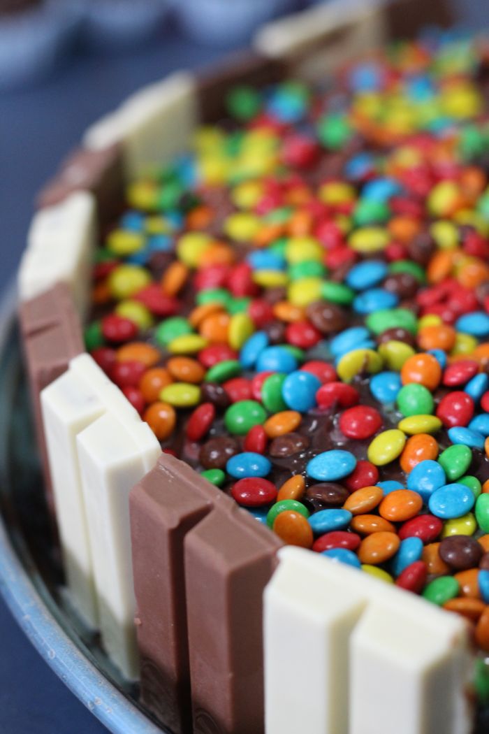 Close-up of a chocolate cake topped with colorful candies and surrounded by chocolate bars.